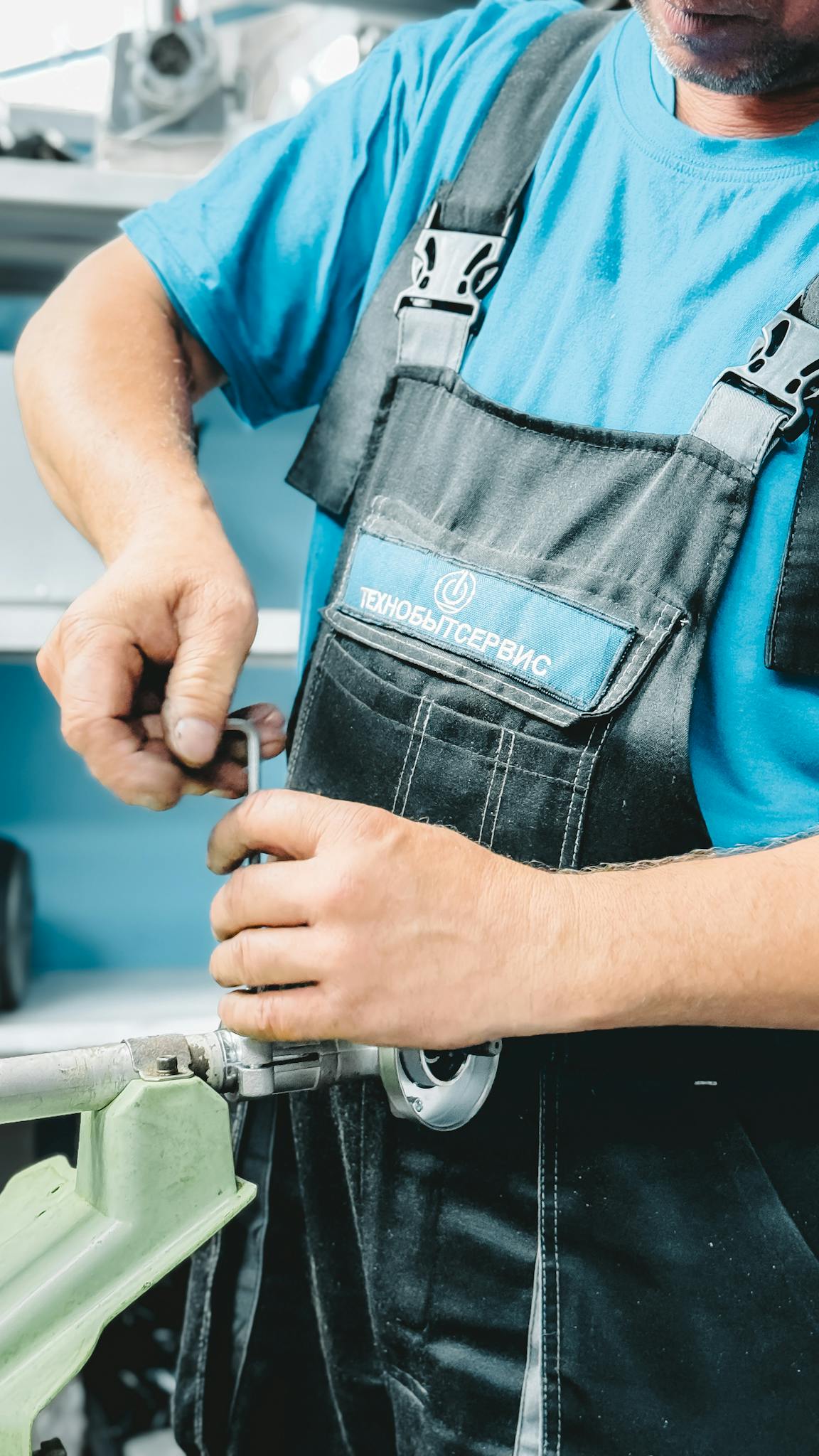 Close-up of a plumber in blue uniform working on a pipe repair with a wrench.
